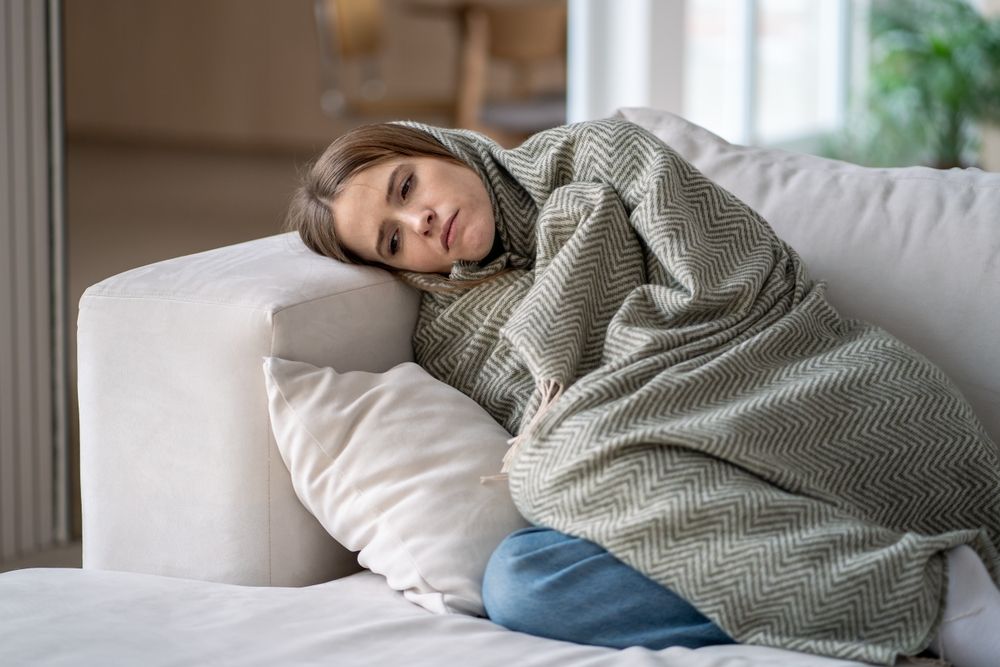 Woman,Lying,On,Couch,Covered,By,Blanket,,Feeling,Emotionally,Drained.