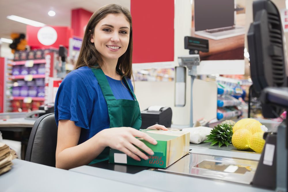 Utánajártunk, mennyi az átlagkereset 2025-ben a bolti eladók esetében a legnagyobb élelmiszerláncoknál. Portrait,Of,Woman,Cashier,Smiling,At,Checkout